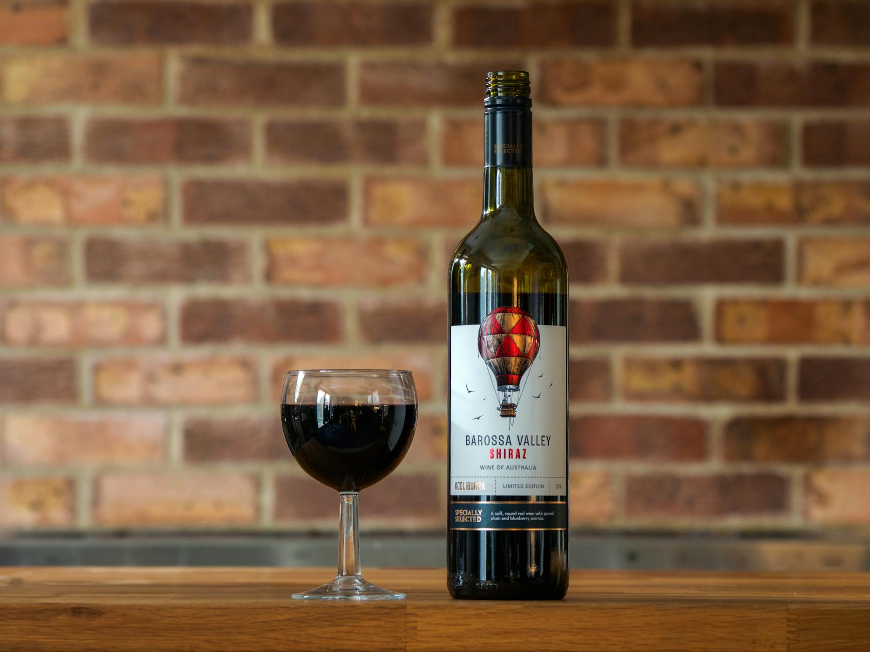 A glass of dark Shiraz red wine in front of vineyard rows