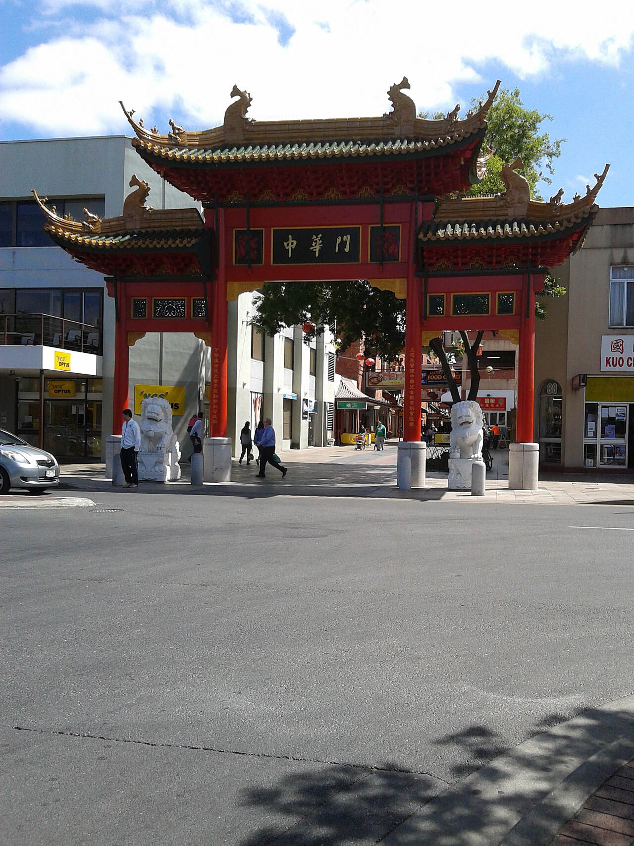 The red Chinatown paifang gate with green-tiled roofs and two white stone guardian lions at the Gouger Street entrance to Moonta Street