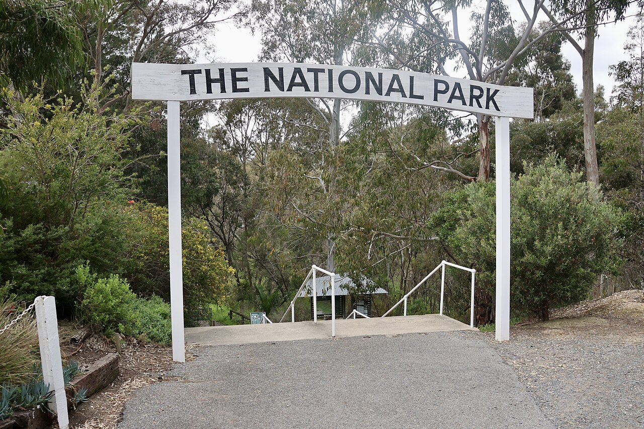 A white archway sign reading The National Park over a path leading into bushland at Belair