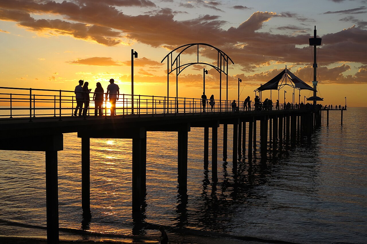 Silhouetted people on Brighton jetty with its arched frames and shelter against a golden sunset over the sea