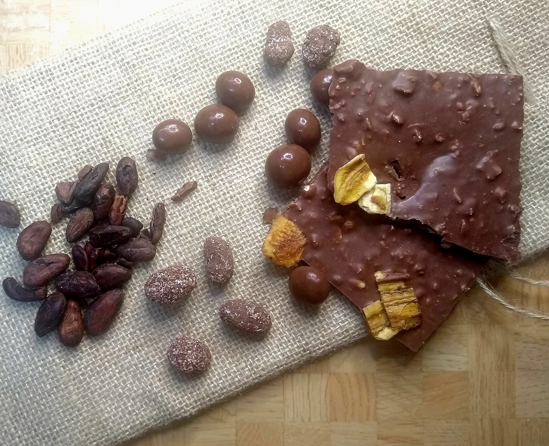 Cocoa beans laid out beside chocolate-coated nuts and broken pieces of chocolate bark
