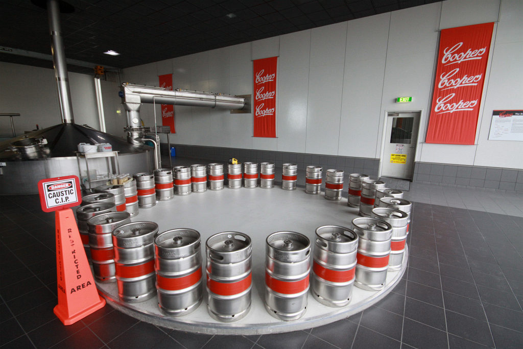 Rows of steel kegs arranged in a ring on the floor of the Coopers brewhouse beneath red Coopers banners