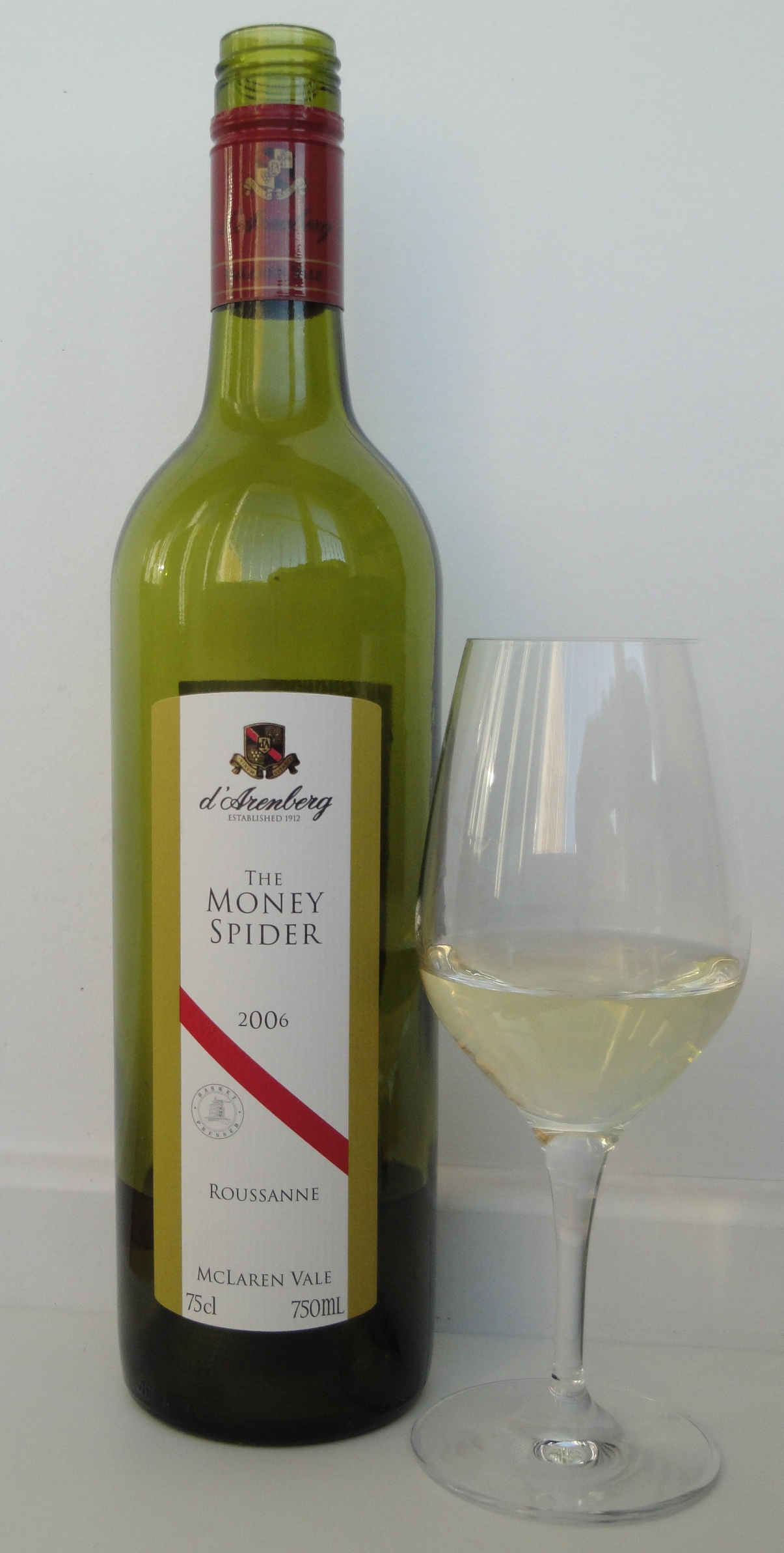 A bottle of d'Arenberg The Money Spider roussanne with its diagonal red stripe label beside a glass of white wine