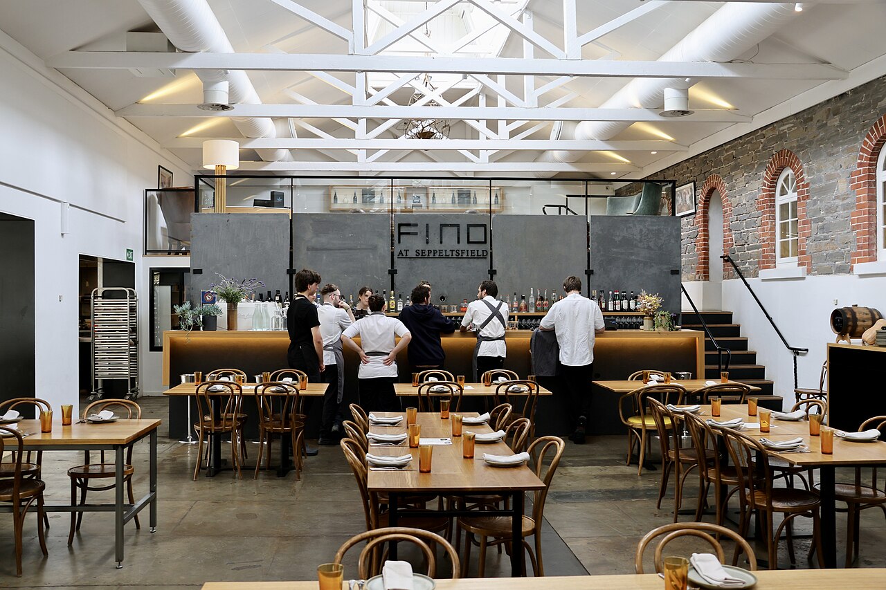 The dining room of FINO at Seppeltsfield with bentwood chairs, set tables, an open kitchen and staff gathered at the pass