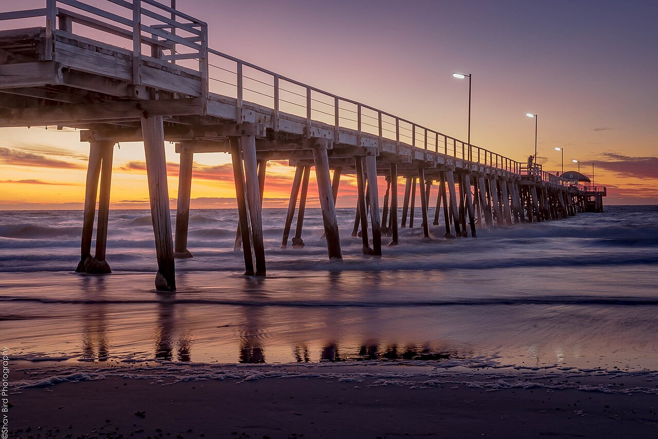 Henley Beach jetty stretching out over calm water at sunset under a pink and orange sky