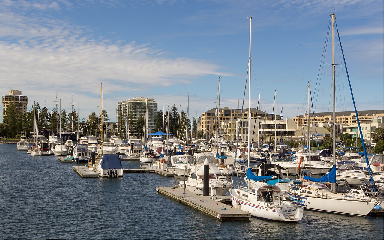 Yachts moored at Holdfast Shores marina in Glenelg with apartment buildings behind under a blue sky
