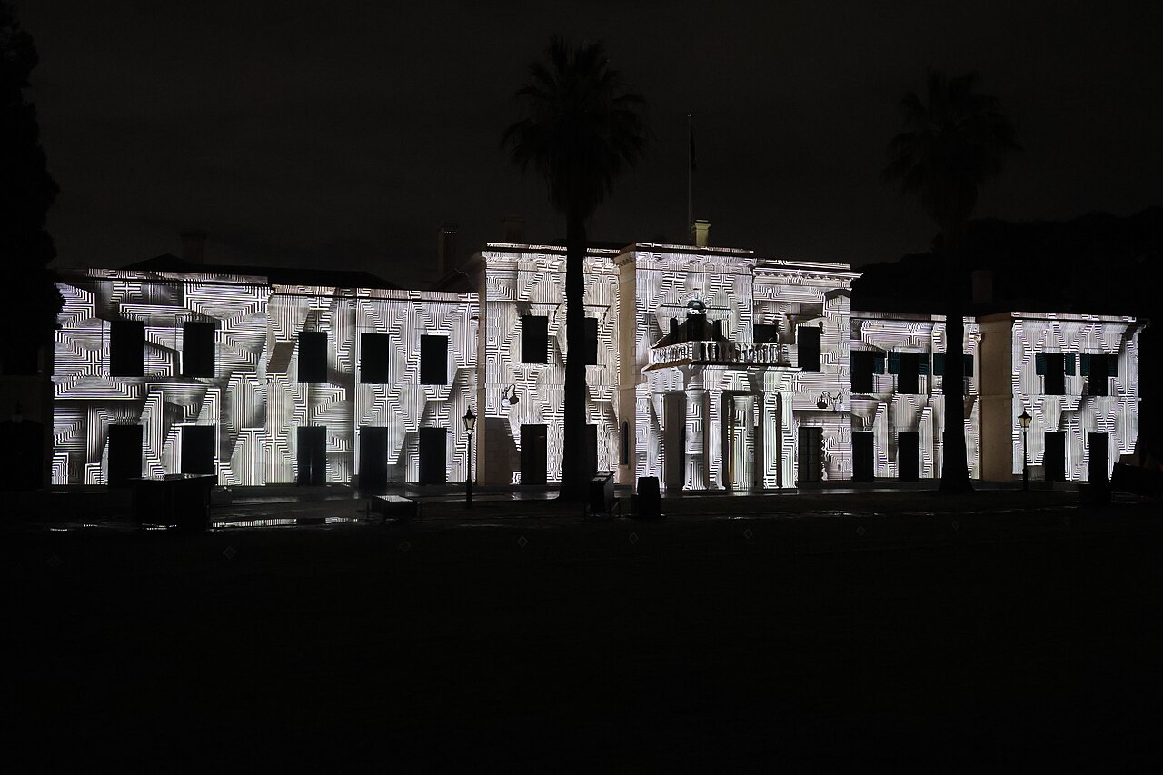 Government House in Adelaide at night with black-and-white geometric patterns projected across its facade, palm trees silhouetted behind
