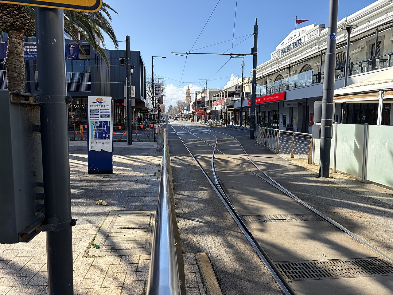 Jetty Road in Glenelg with tram tracks running between shops and cafés towards the town hall clock tower