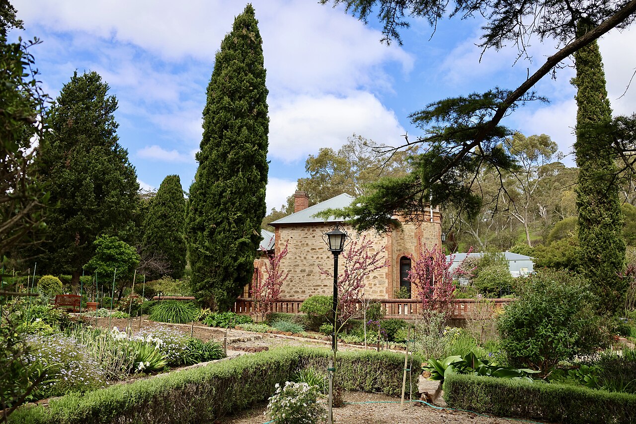Old Government House at Belair, a stone house behind formal gardens with clipped hedges and tall conifers