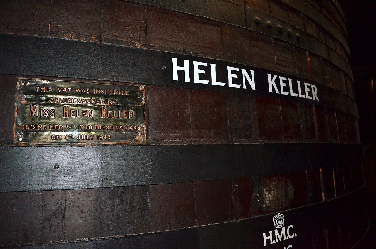 A huge dark wooden wine vat painted with the name Helen Keller and a brass plaque recording her visit to the cellars in 1948
