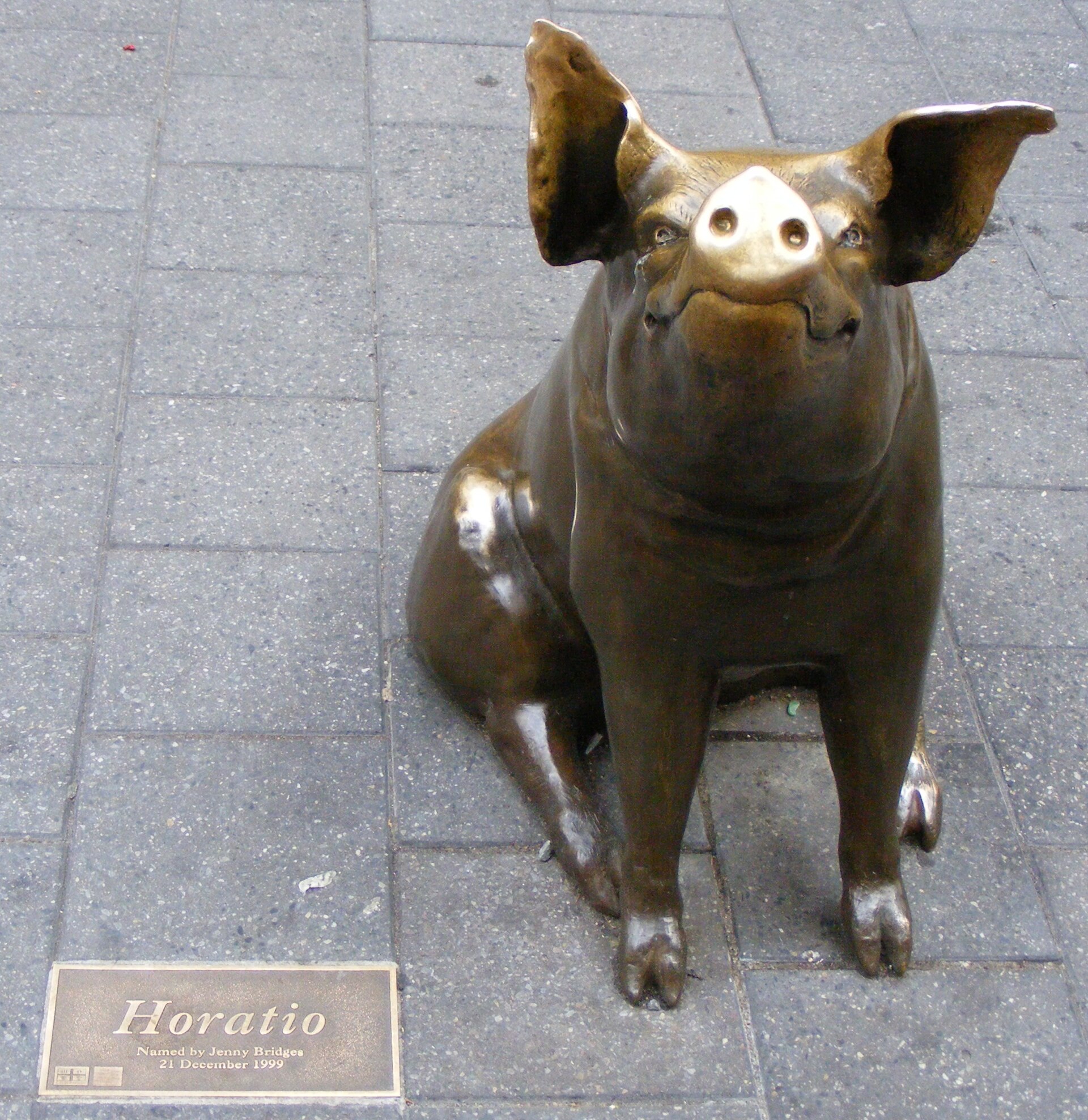 Horatio, a seated bronze pig with polished ears and snout, beside his name plaque set into the paving