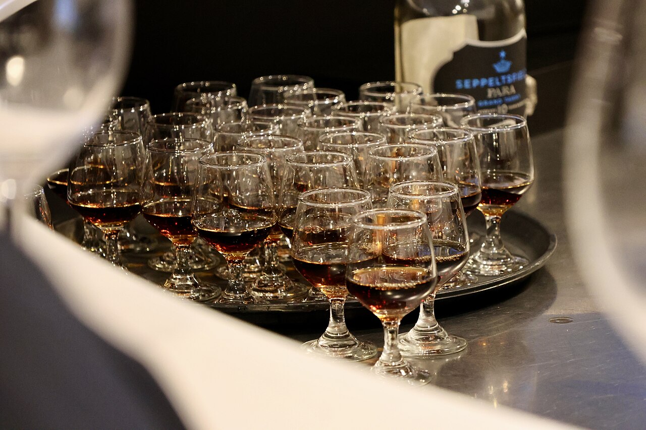 A tray crowded with small stemmed glasses of amber tawny wine beside a bottle of Seppeltsfield Para