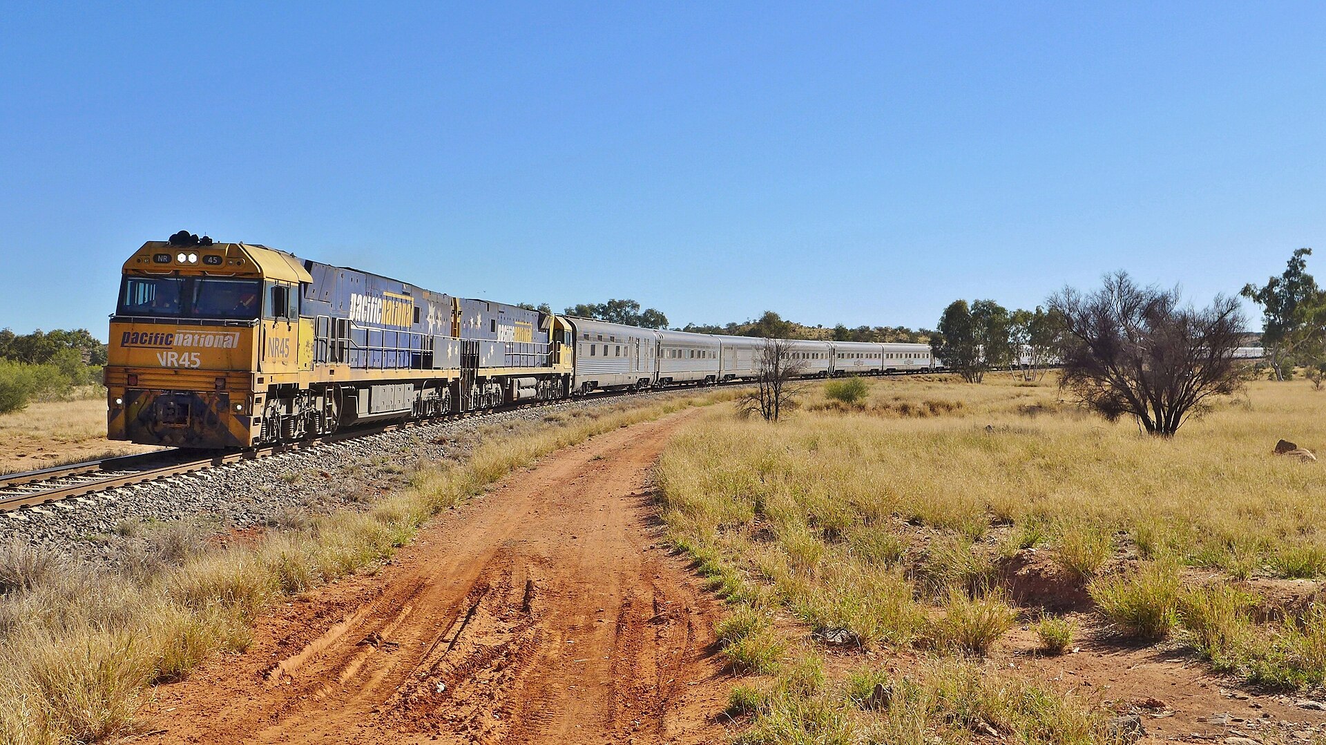 The Ghan passenger train with two locomotives crossing red outback country in central Australia