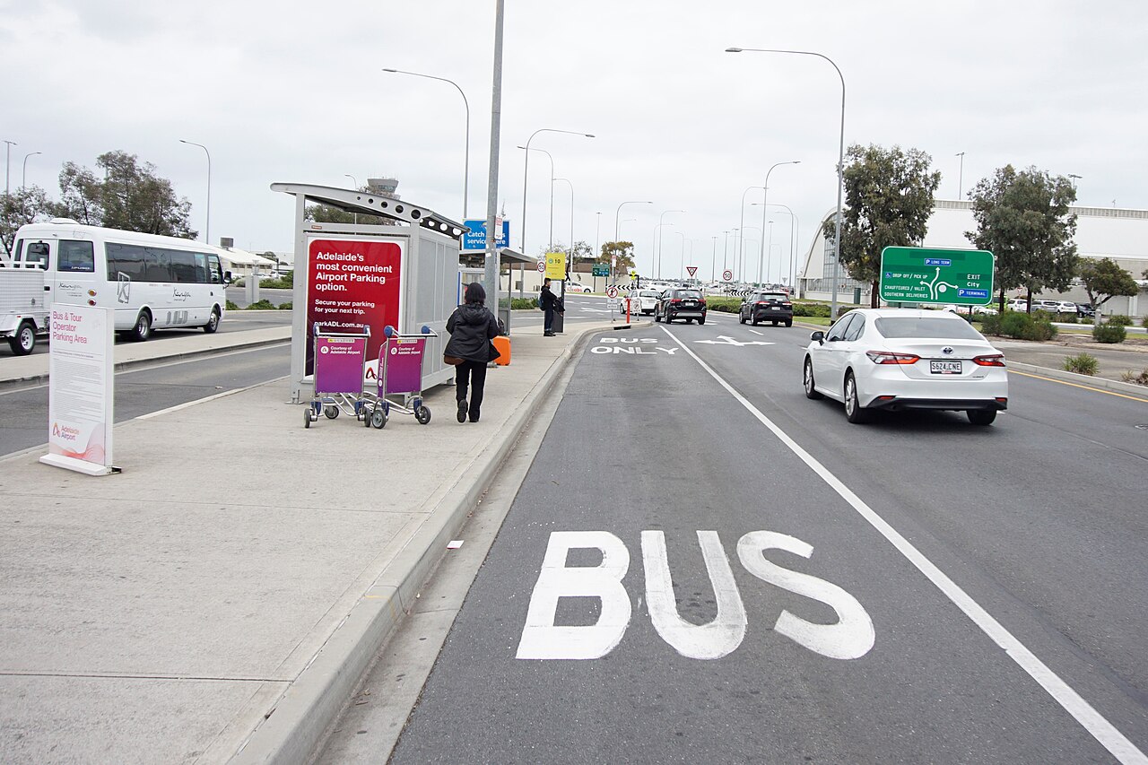 The bus stop outside Adelaide Airport, with a shelter, luggage trolleys and a marked bus lane on the road in front of the terminal