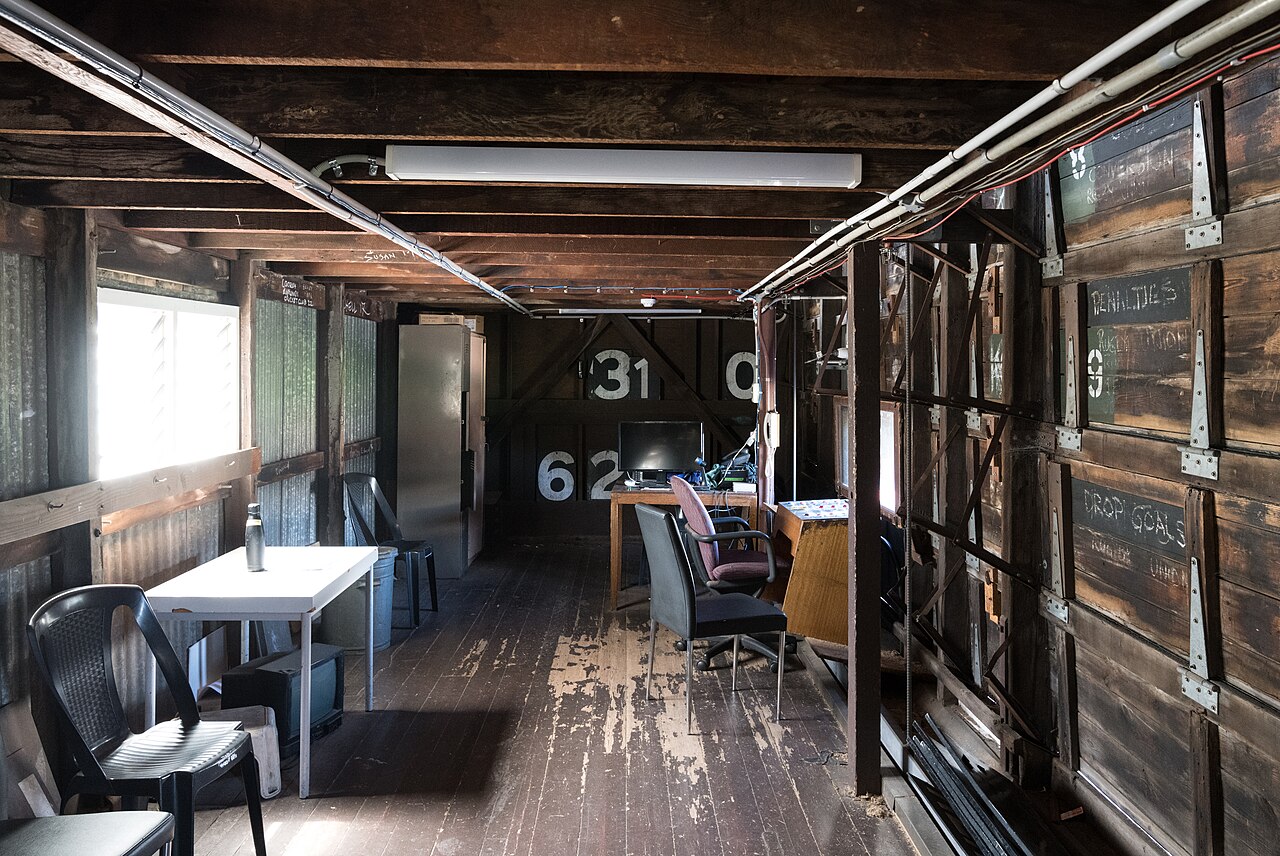 Inside the heritage scoreboard at Adelaide Oval, a narrow wooden room with large painted number boards, a table and chairs and windows onto the ground