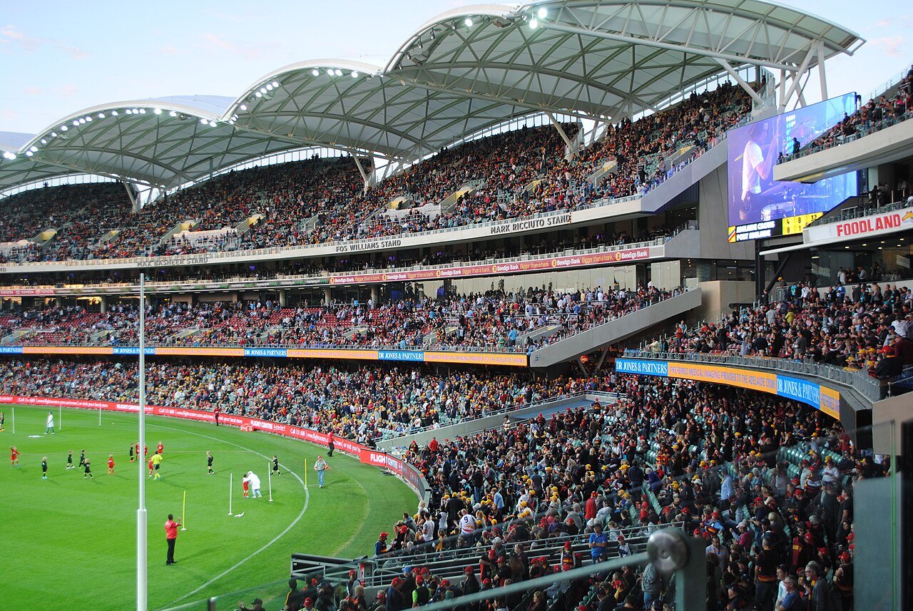Packed stands at Adelaide Oval during the half-time break of a Showdown between Adelaide and Port Adelaide, with the stadium's curved roof canopies and big screen