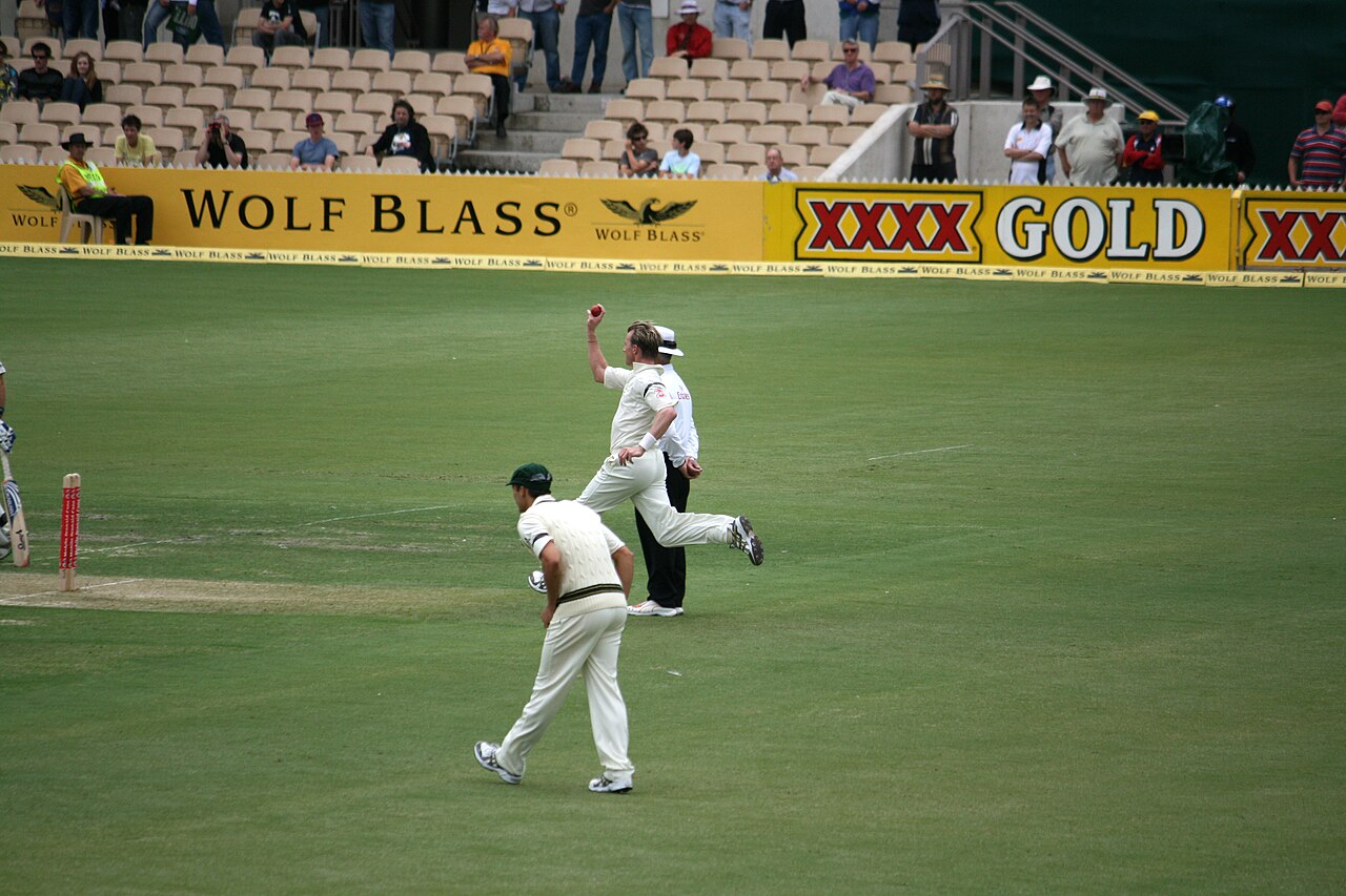 Fast bowler Brett Lee in full stride after delivering the ball during a Test match at Adelaide Oval, with the umpire and the crowd in the stands behind