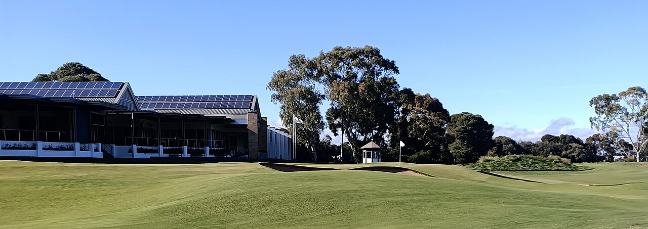 The modern clubhouse at Kooyonga Golf Club with solar panels on its roof, looking across a manicured fairway and green towards gum trees