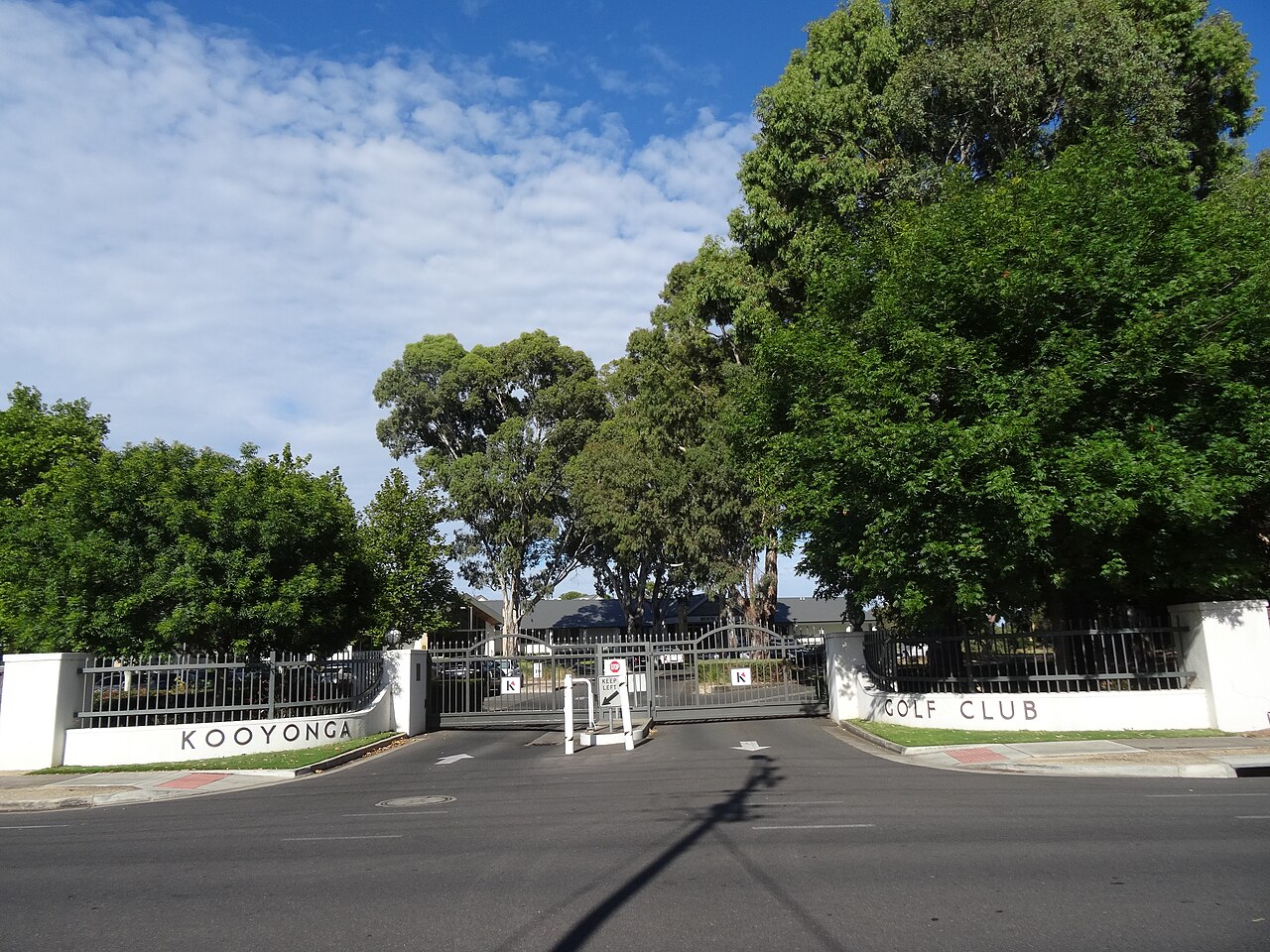 The entrance gates of Kooyonga Golf Club on May Terrace, with white walls lettered Kooyonga Golf Club and large trees behind