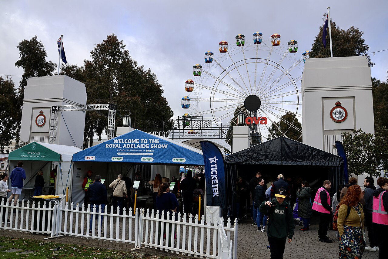 The entrance to the Royal Adelaide Show at Wayville in 2025, with white gate pillars, a blue Welcome to the Royal Adelaide Show tent and the Ferris wheel behind