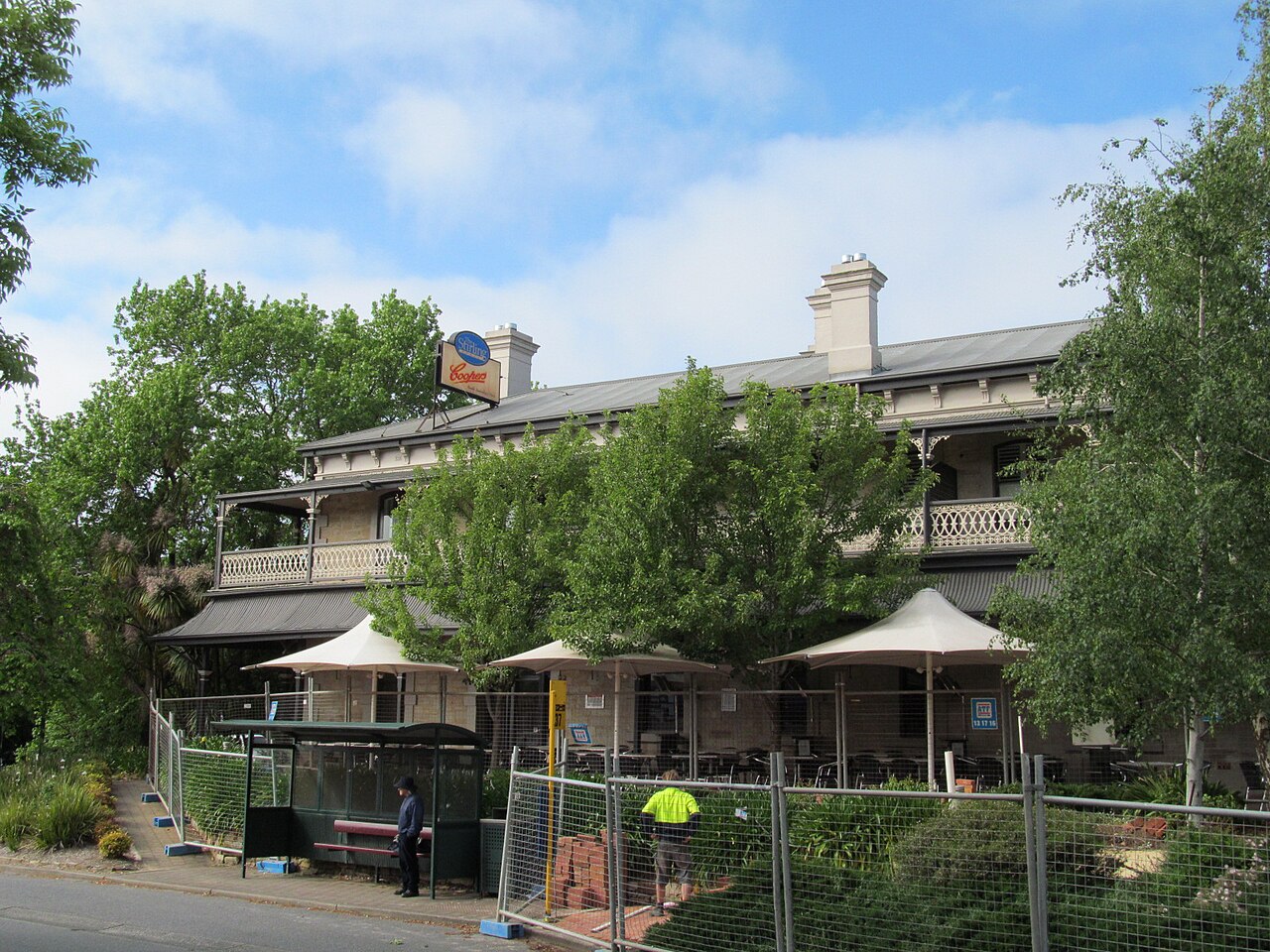 The two-storey Stirling Hotel in the Adelaide Hills, with an iron-lace balcony, outdoor umbrellas and leafy trees along the street